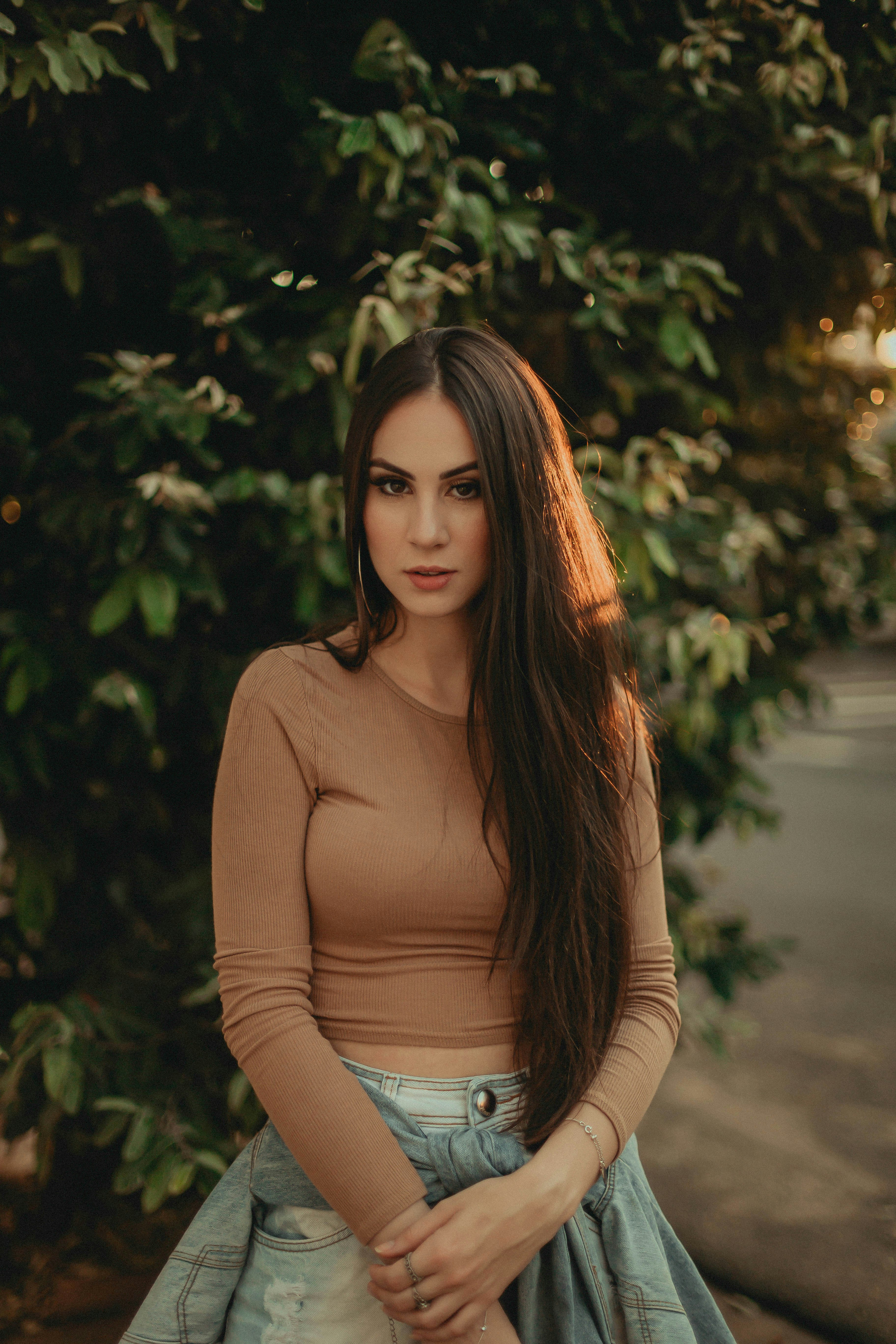 woman in brown long sleeve shirt standing near green tree during daytime